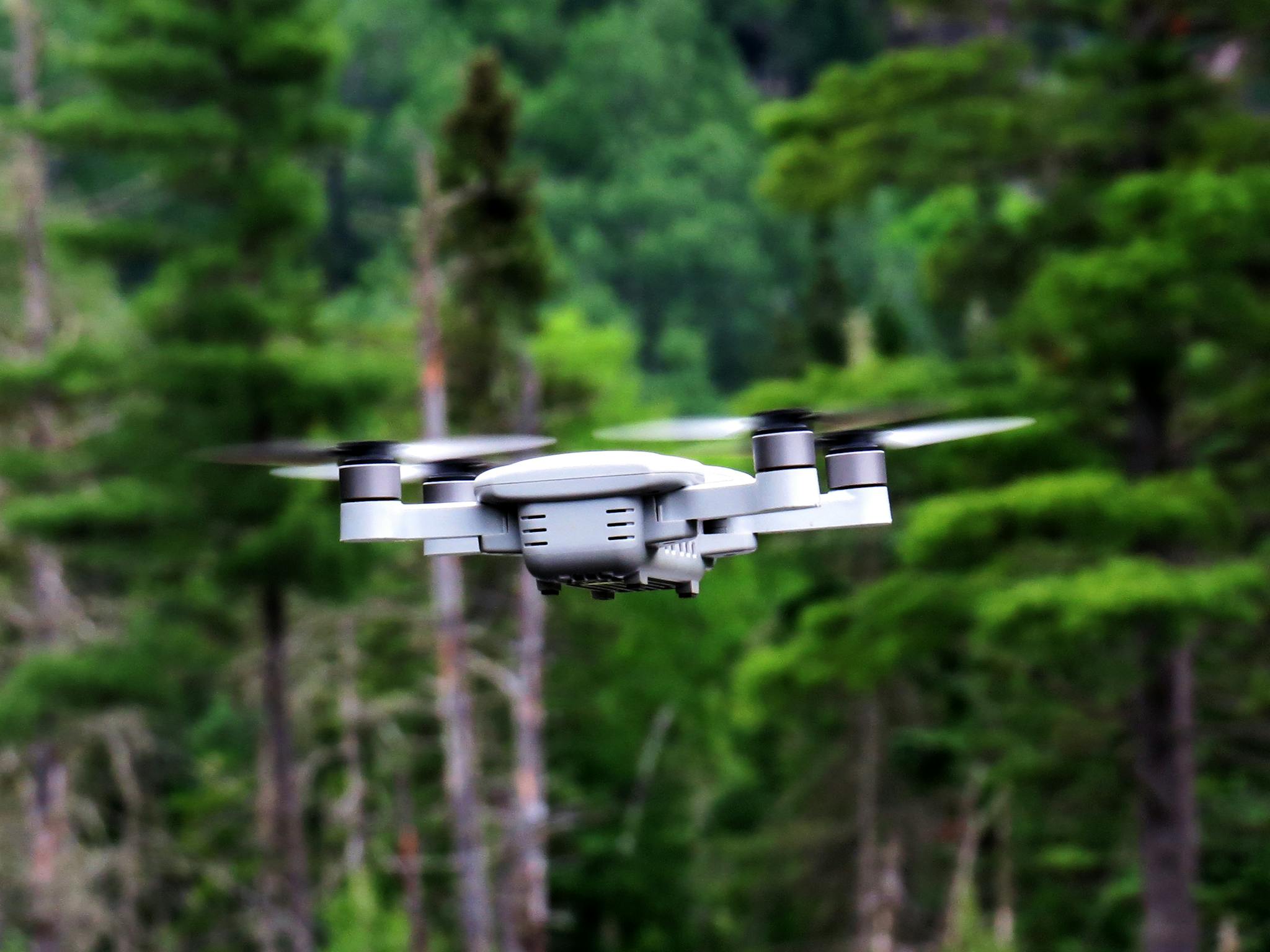 High-tech drone flying in lush green forest showcasing modern technology in nature.